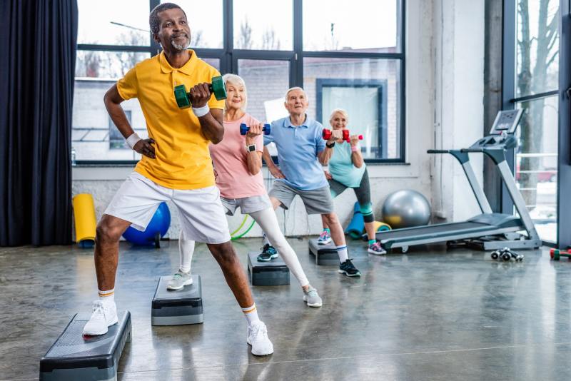 multicultural senior sportspeople synchronous exercising with dumbbells on step platforms at gym